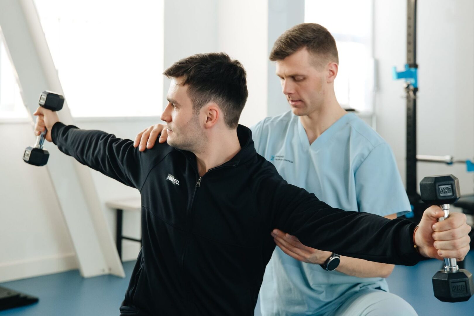 Fysiotherapeut begeleidt een schouderoefening met dumbbells